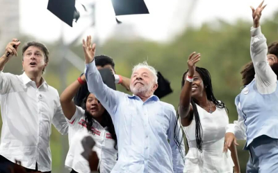 Imagem mostra Lula ao lado de esatudantes enquanto jogam capelos para cima