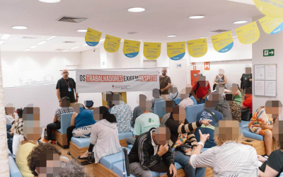 Imagem mostra dirigente do sindicato estendendo faixa onde se lê "os trabalhadores exigem respeito" dentro de uma agência superlotada do Banco do Brasil