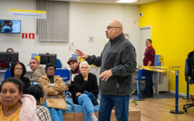 Imagem mostra o dirigente sindical João Maia (um homem branco, careca e de cerca de 50 anos), conversando com populares dentro de uma agência lotada do Banco do Brasil