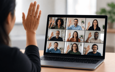 imagem mostra mulher com a mão levantada em frente a uma tela de computador em cuja tela são projetadas diversos rostos de pessoas em uma reunião virtual