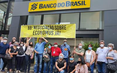 Imagem mostra funcionários e aposentandos do Banco do Brasil oriundos de bancos incorporados, em frente à sede do Banco do Brasil, segurando uma faixa com os dizeres: BB: negociação sobre Economus Já