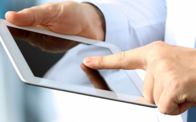 Foto mostra homem de pele branca e camisa azul clara mexendo em um tablet. A foto está focando no aparelho e nas mãos da pessoa