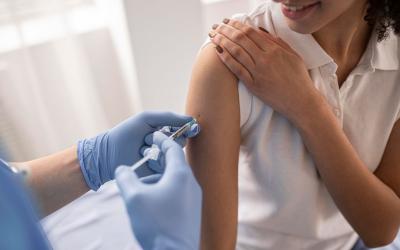 Mulher negra recebe dose de vacina em seu braço direito, aplicado por mulher branca