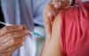 Foto em que aparece o braço de uma pessoa e as mãos de um profissional de saúde preparando-se para aplicar uma injeção