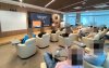 Imagem mostra uma sala cheia de pessoas. Elas estão sentadas em poltronas e de frente para um pequeno palco