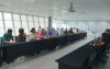 Imagem mostra sala onde ocorreu a reunião para discutir o Saúde Caixa. a imagem mostra 12 pessoas sentadas lado a lado em uma mesa comprida. Atrás dela há uma janela que ocupa toda a parede. 