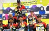 Fotografia mostra participantes do torneio de pesca com camisa colorida de vermelha, amarelo e preto segurando troféu nas mãos