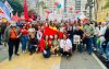 Homens e mulheres usando vermelho, alguns agachados e de fundo bandeiras de partidos e centrais sindicais