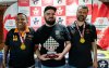 fotografia mostra 3 homens brancos cegos, com camisa preta, um deles boné e medalha de participação no peito