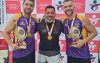 Fotografia mostra 3 homens brancos de camiseta roxa e preta segurando troféu nas mãos