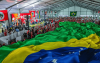 Foto mostra grande bandeira do Brasil sobre grande parte dos presentes em auditório onde ocorreu encerramento do encontro do MST