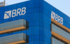 Imagem mostra o alto da fachada do prédio do BRB. o edifício é espelhado com vidros azuis. a imagem foca no lato da fachada, que exibe o logo do banco