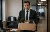Imagem de um homem de terno segurando seus pertences de trabalho em uma caixa de papelão