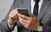 Imagem mostra um homem vestido de terno e gravata mexendo no telefone celular