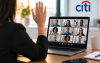 Imagem mostra uma mulher em frente a um computador e com a mão levantada