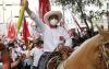 Usando máscara em decorrência da pandemia de Covid-19 e chapéu tradicional, presidente eleito do Peru, Pedro Castillo, ergue o braço montado em um cavalo cor de caramelo com apoiadores ao fundo